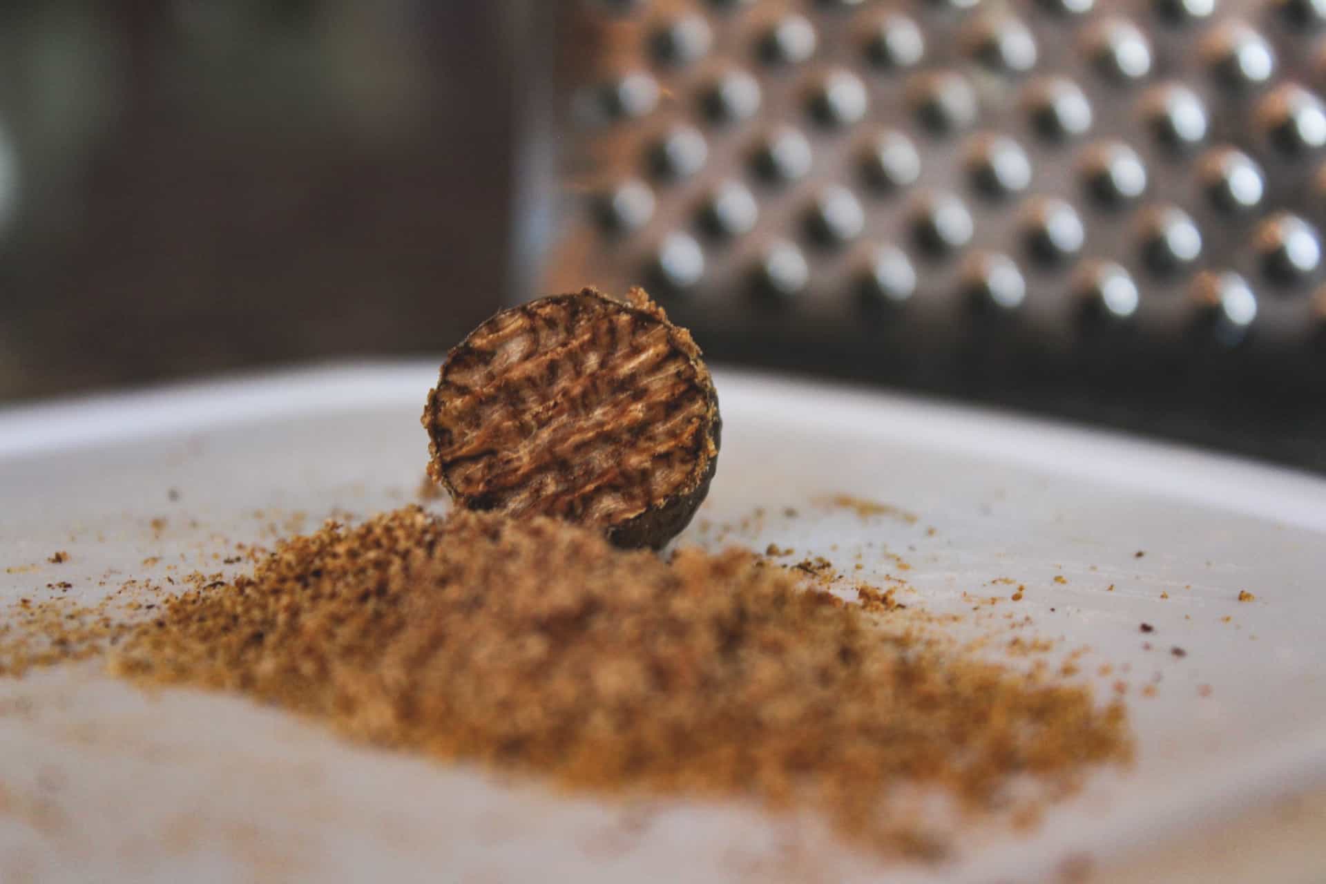 grated nutmeg on a cutting board with a grater in the background