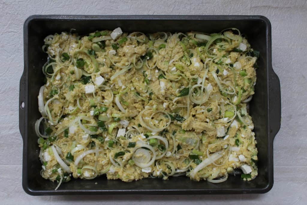 Raw Pispili in a pan with leeks on top 
