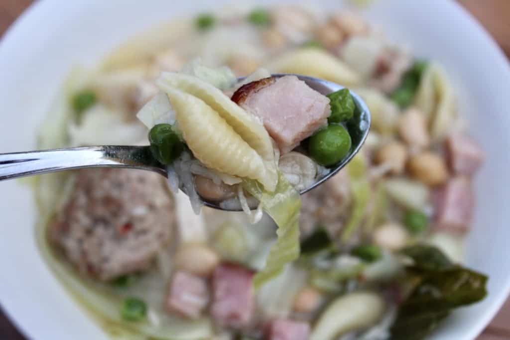 View of spoon filled with ham, peas, and noodles 