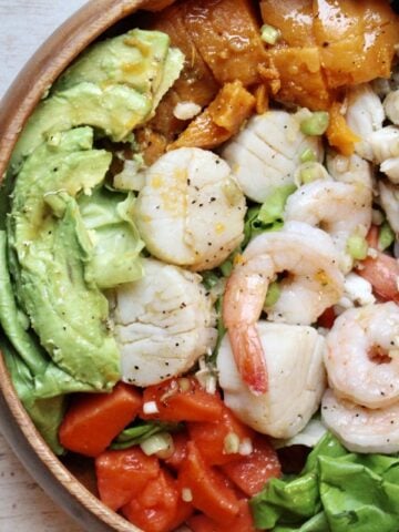 A seafood salad with avocado slices and tomatoes served over a bed of lettuce.