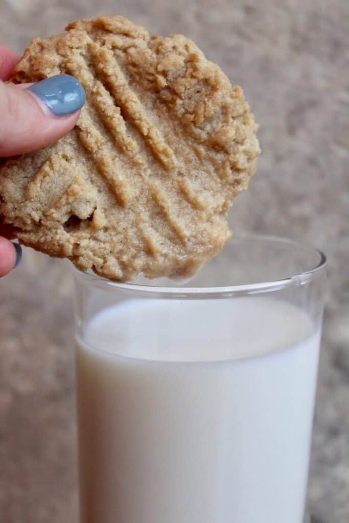 A hand dipping a tahini cookie in milk.