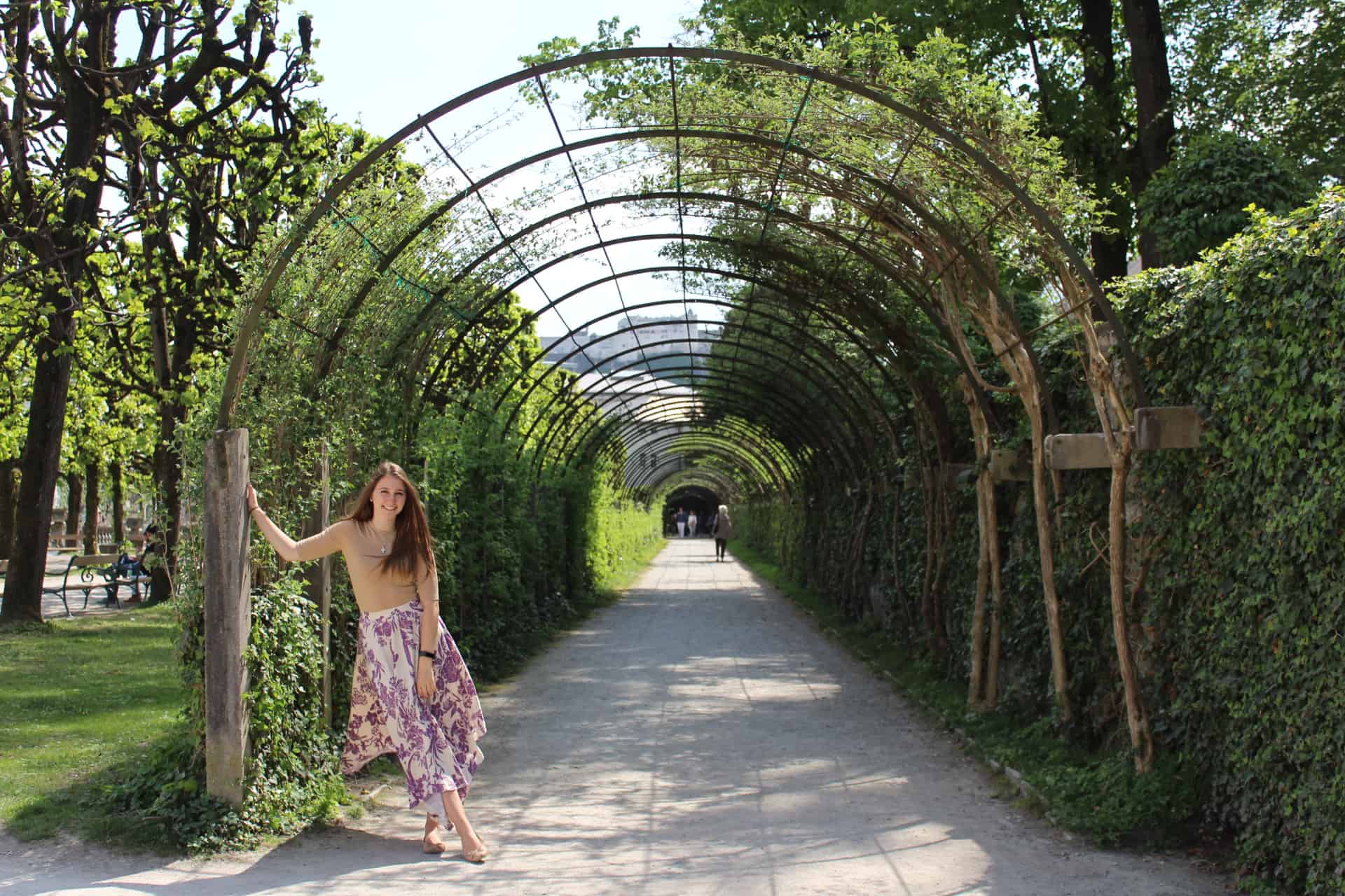 A girl standing in front of an arch in a garden.