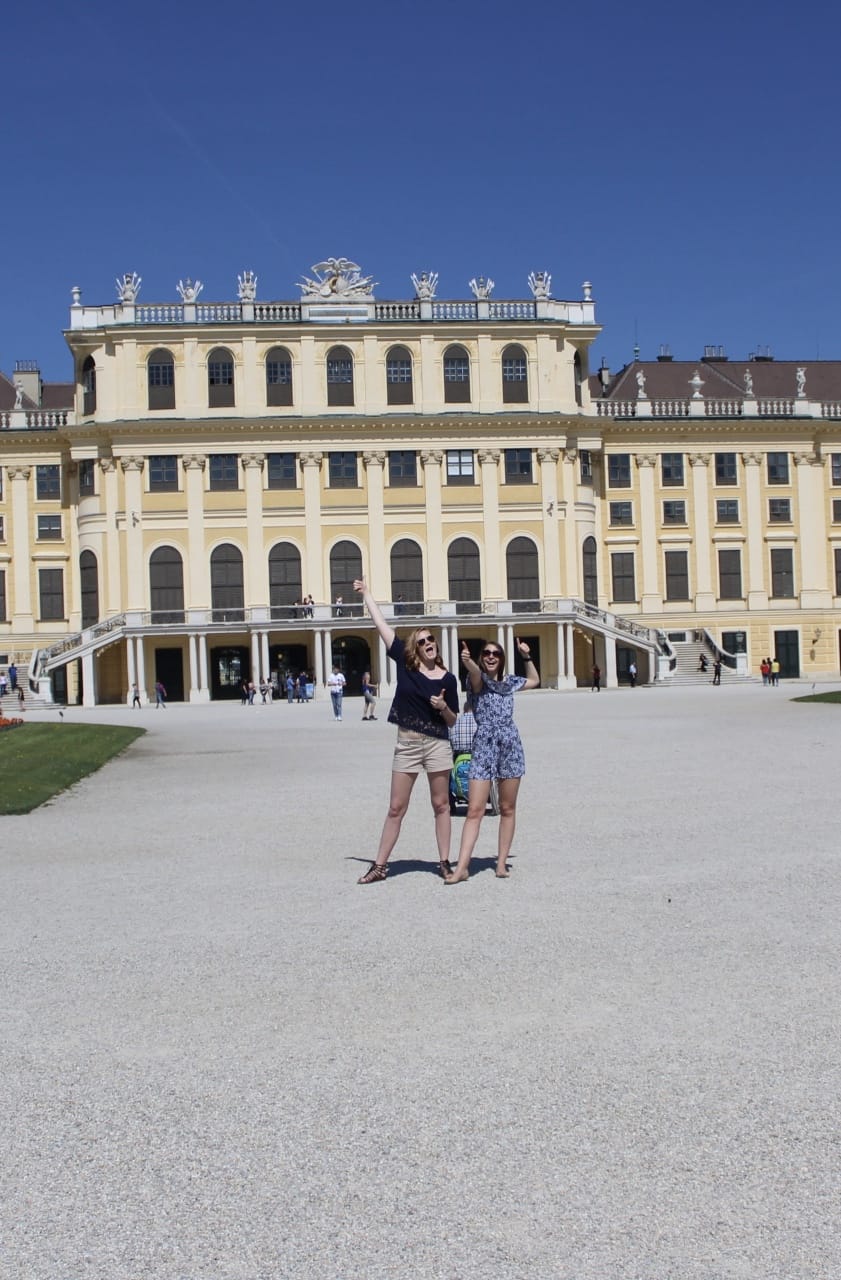 Two girls giving a thumbs up in front of an Austrian palace.
