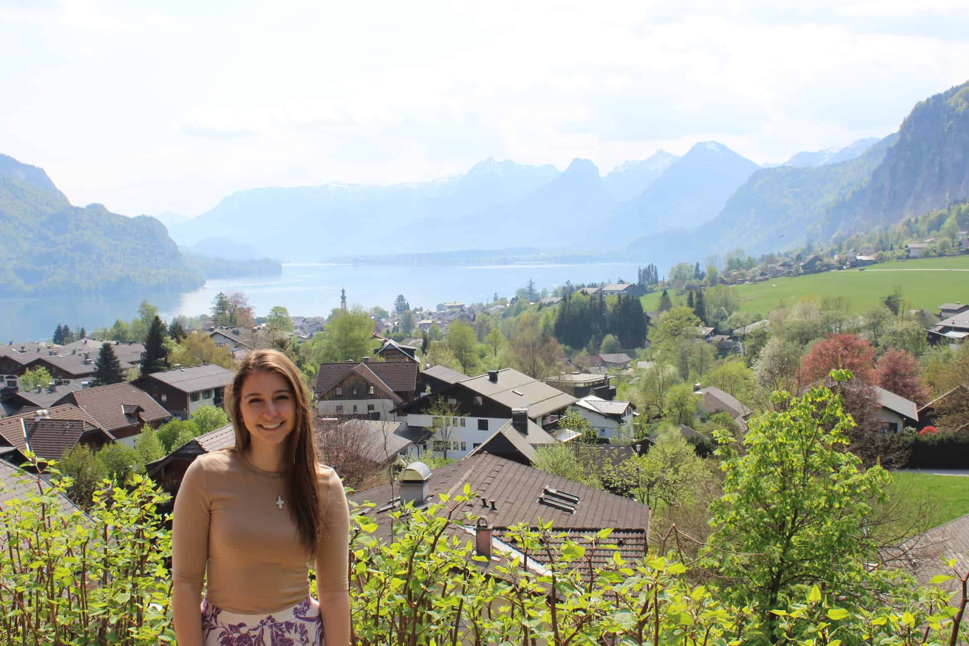 A girl standing in front of the Austrian alps and a village in the valley.