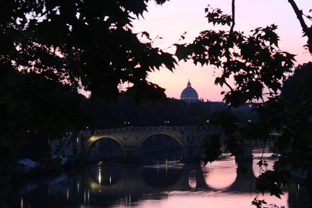 pink sunset over a river in rome with St Peter's Basilica in the background.