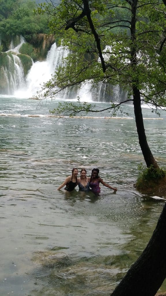3 girls standing in water in front of the krka waterfalls