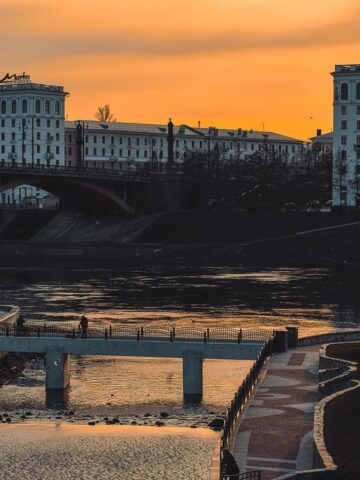 A river scene in Belarus at sunset with two bridges in the distance.
