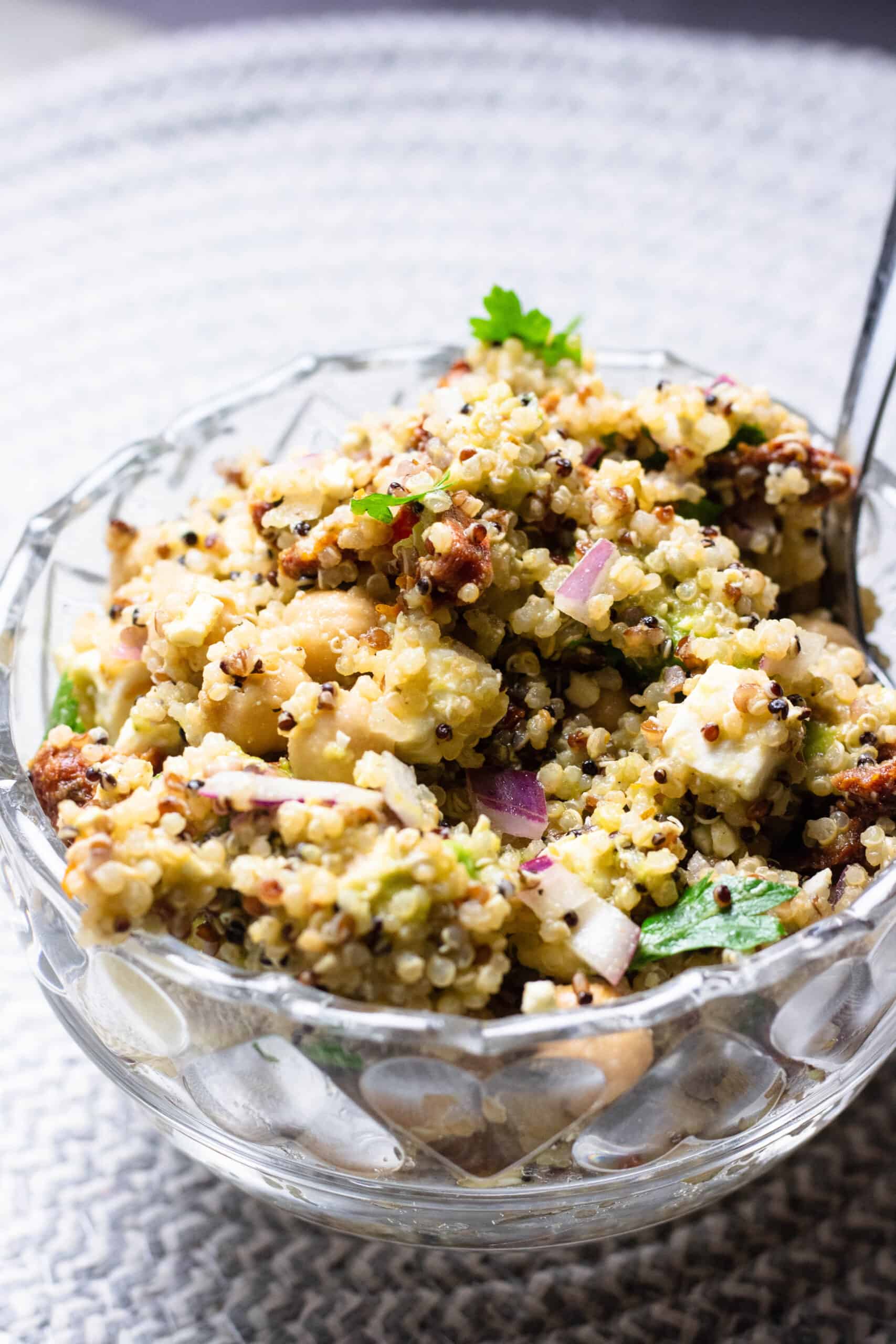 Quinoa salad in a glass bowl mixed with red onions, cheese, and chickpeas.