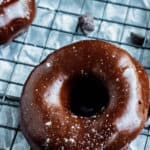 Chocolate glazed donuts on a drying rack covered in melted chocolate and sprinkled with powdered sugar.