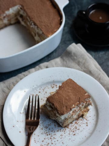 The best Tiramisu recipe. Tiramisu on a plate with a large pan of it in the background