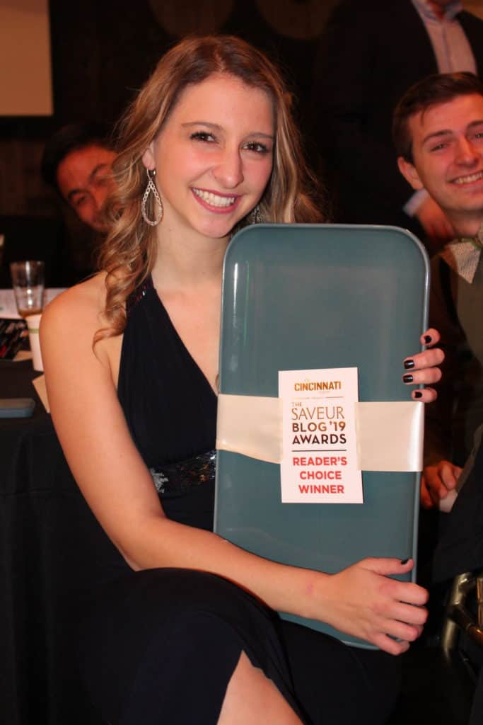 A girl holding a award with two guys smiling behind her. 