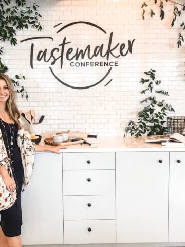 A girl posing in front of a kitchen set with the sign "tastemaker Conference".