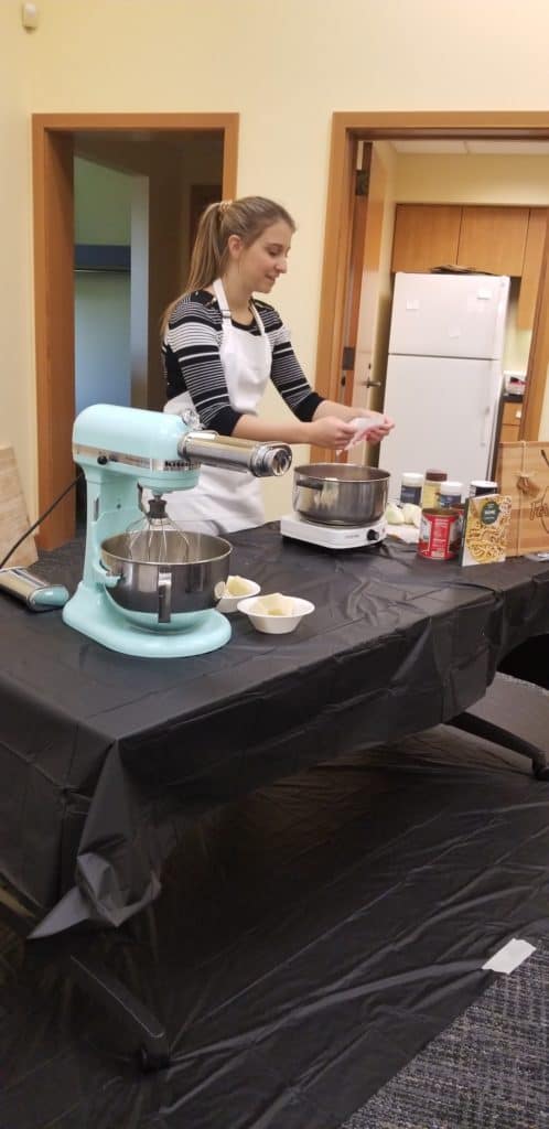 a girl teaching a cooking class in front of a stand mixer and a large pot. 