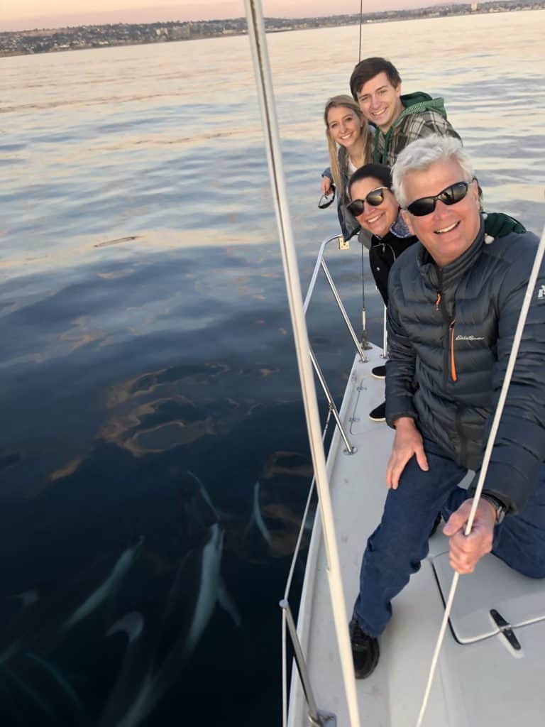 a gamily posing on a sailboat with dolphins in the water. 