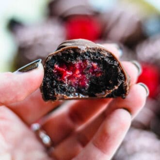 A hand holding a raspberry oreo truffle covered in chocolate.