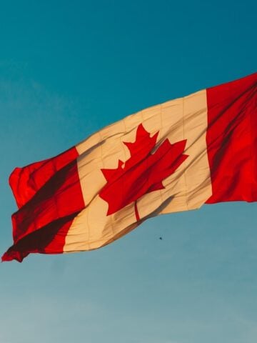 Canadian flag flying on a blue sky.