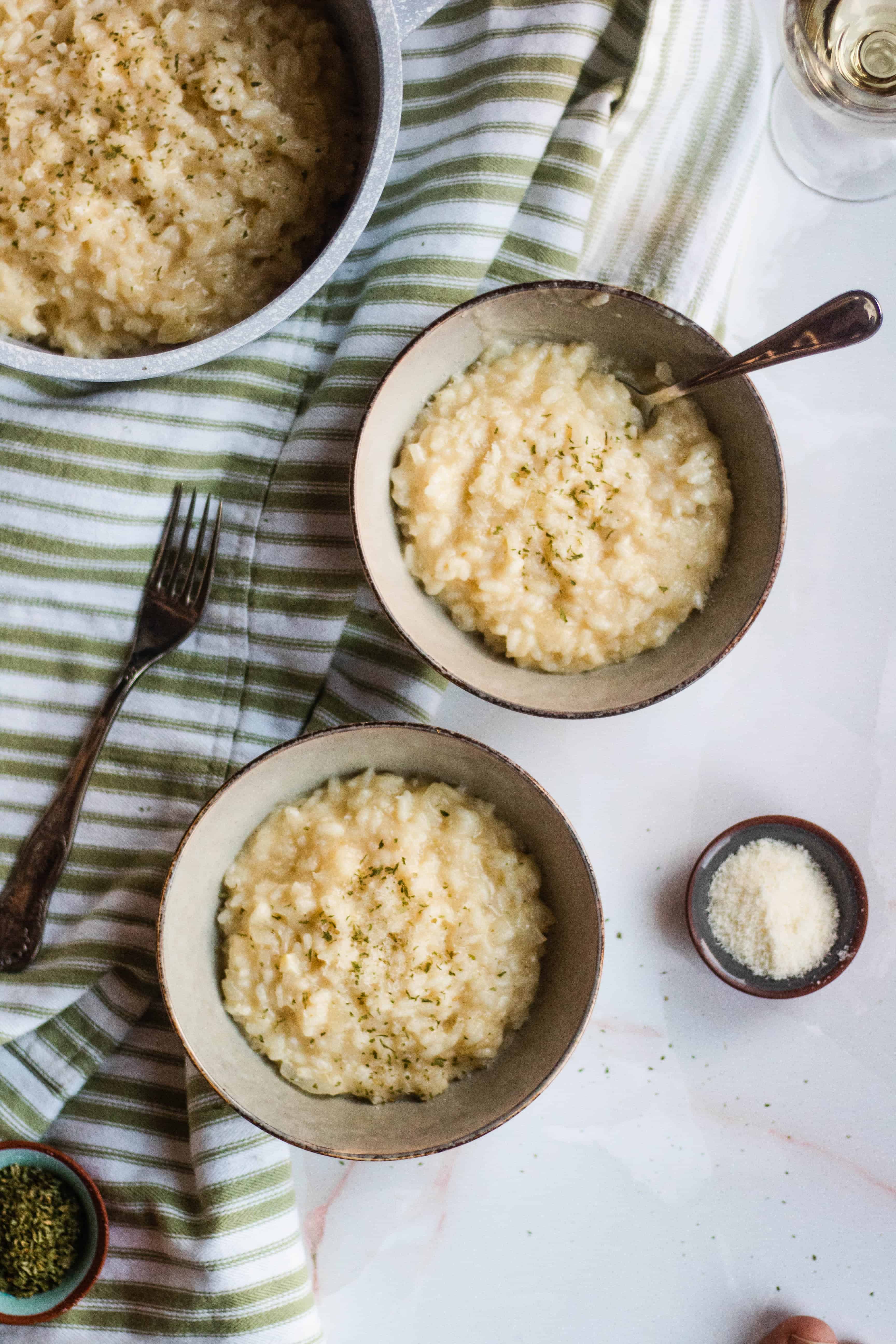 Two bowls of Parmesan risotto with a small bowl of parmesan cheese next to them.