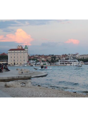 A sunset in Croatia over the ocean with buildings and boats in the background.
