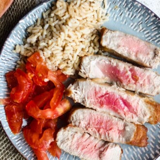 Tuna steak on a plate with tomatoes and brown rice on the side.