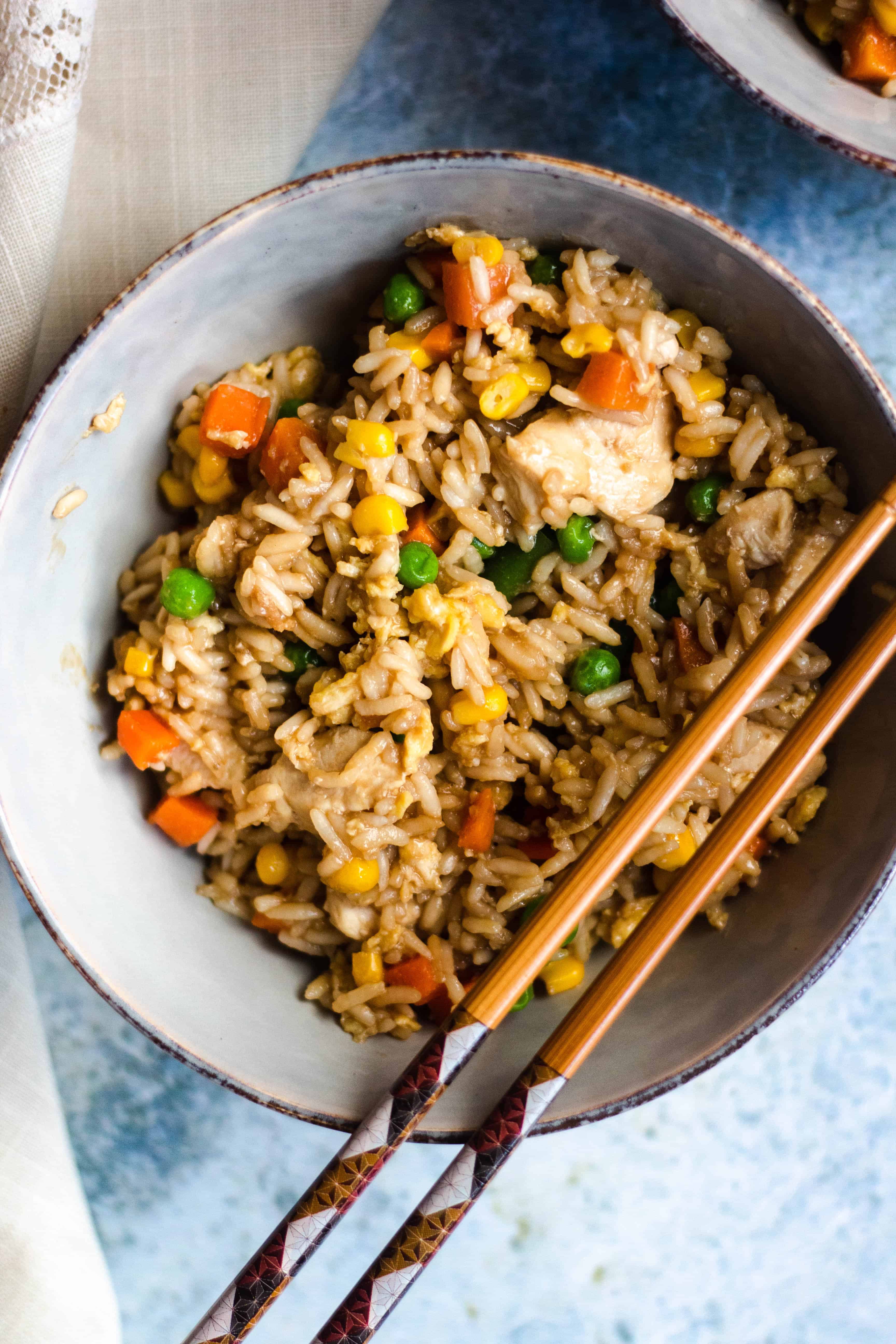 Bowl of chicken fried rice with a pair of chopsticks laying over the bowl. 