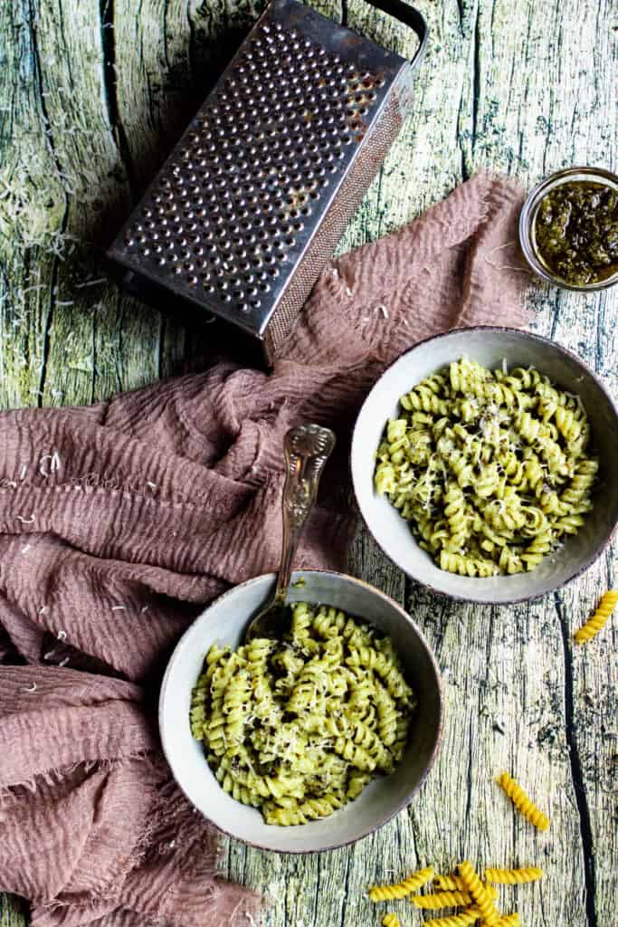 creamy pesto pasta with a cheese grater and serving rag 
