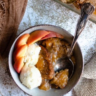Bowl of homemade peach cobbler with a spoon scooping a bite