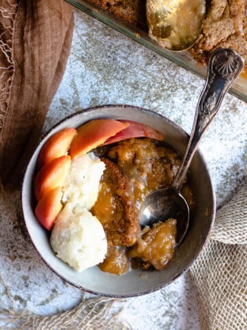 Bowl of homemade peach cobbler with a spoon scooping a bite