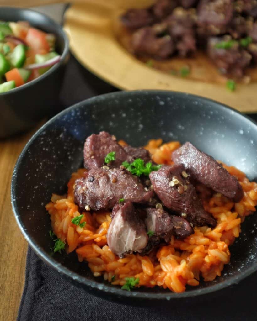 Black bowl with orange rice and slices of meat 