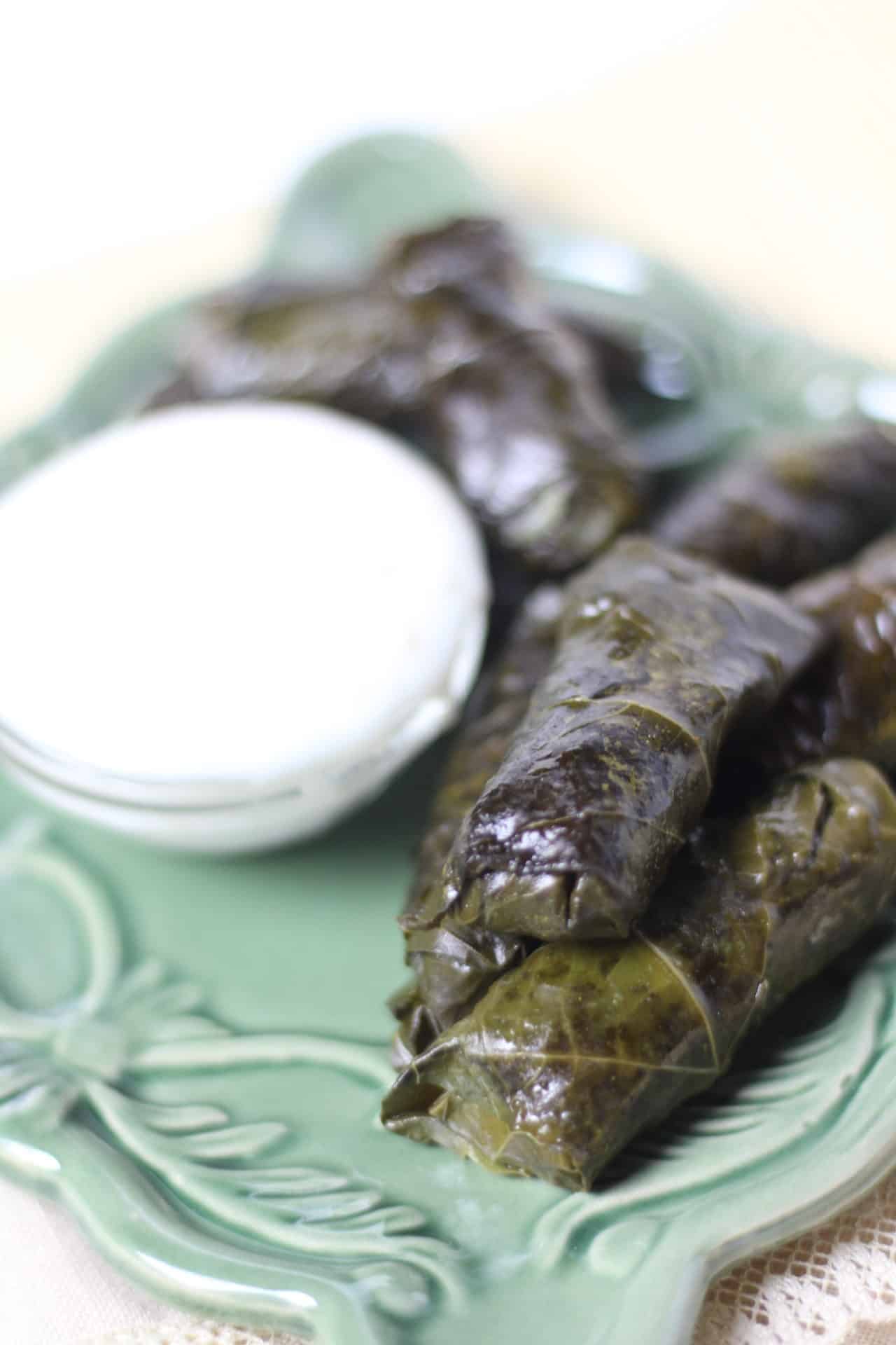 Stuffed grape leaves on a platter with a sauce in a bowl. 