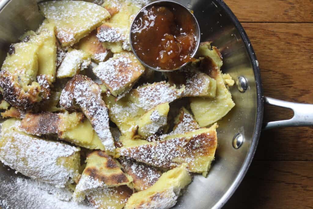 Overhead view of Kaiserschmarrn in a skillet with jam dipper