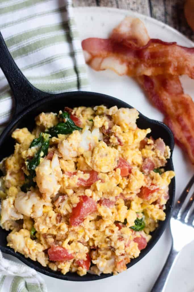 Small skillet full of lobster BLT scrambled eggs with bacon on the side