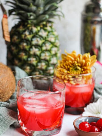 A glass of a Bahama Mama cocktail with maraschino cherries, pineapples, and flowers as decorations.