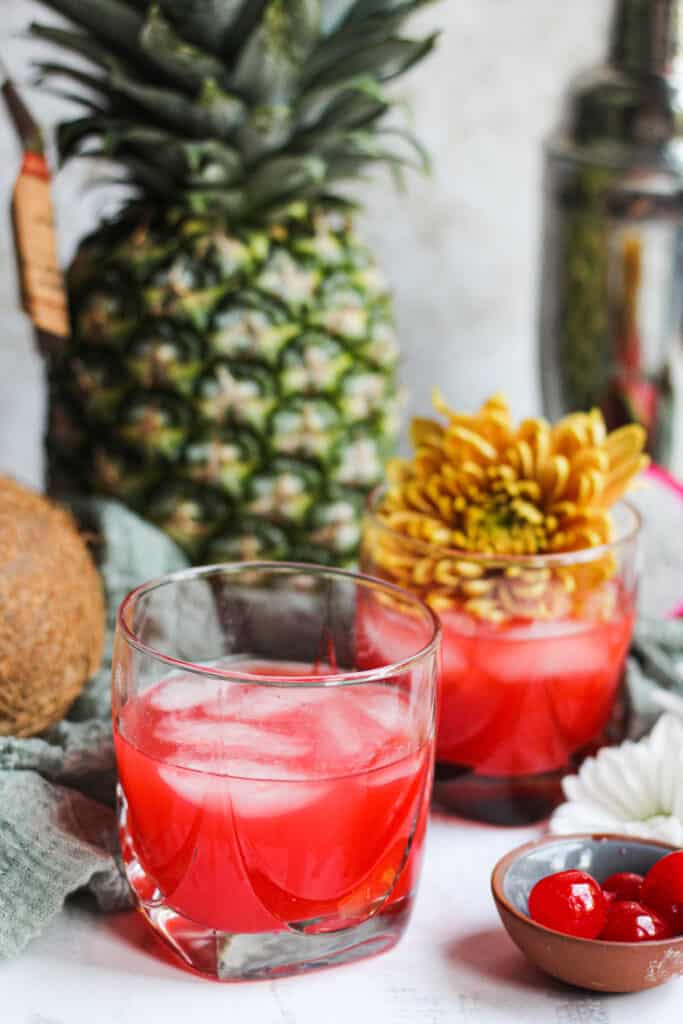 Two glasses of Bahama Mama with Pineapple and Flowers in the background 