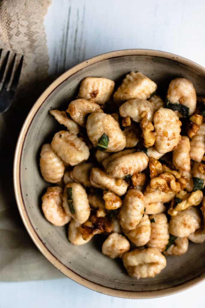 Bowl of brown butter gnocchi with walnut pieces and sage 