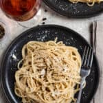 Black plate with Cacio e Pepe, a fork, and a glass of rose
