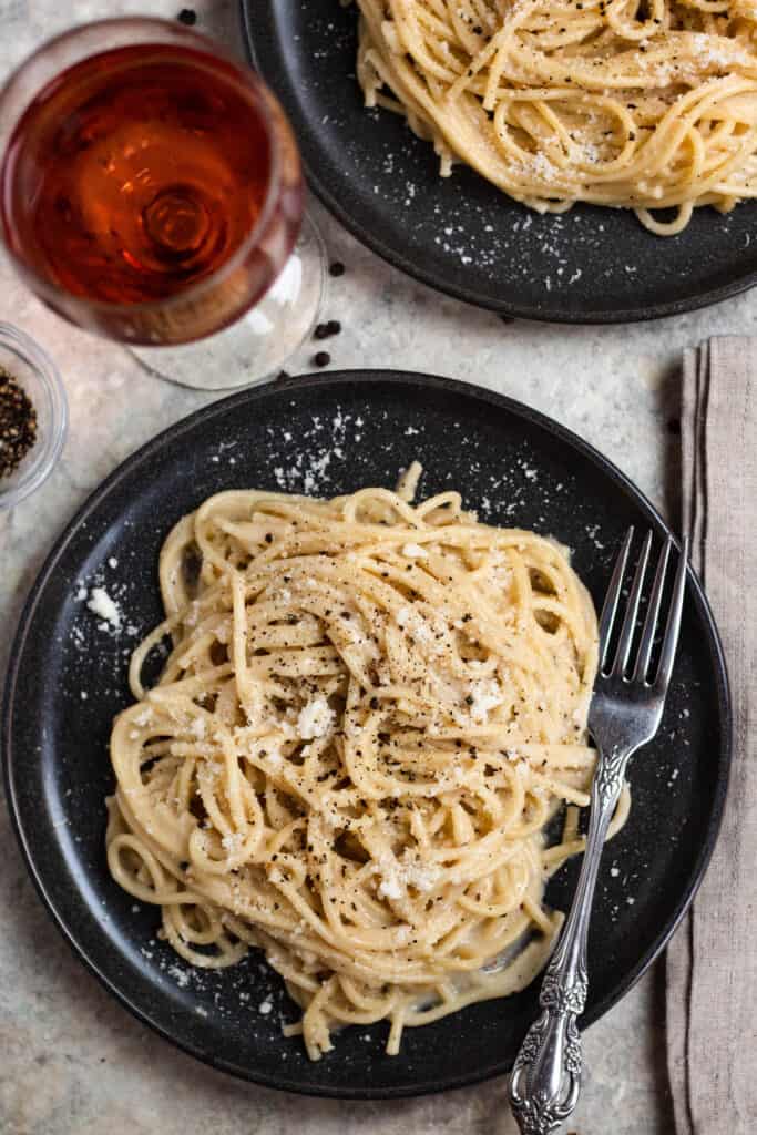 Overhead view of a plate of Cacio e Pepe with a glass of wine and a fork