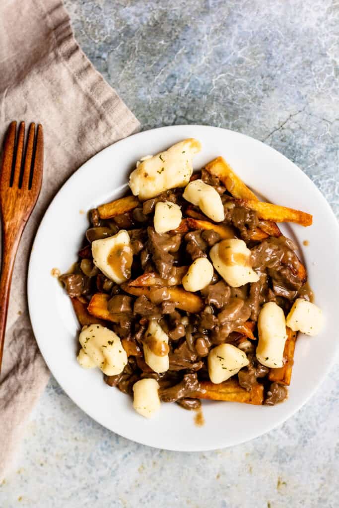 Overhead view of a plate of poutine with a wooden fork next to it