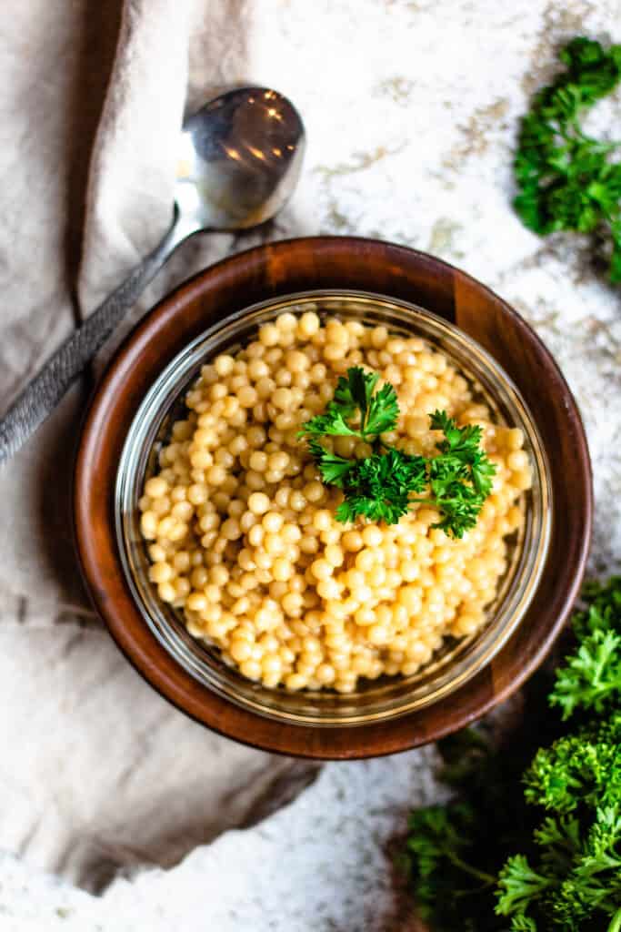 Overhead shot of couscous with parsley and a spoon in a wooden bowl