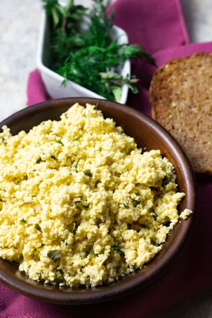 Vertical photo that features scrambled eggs with dill and crusty bread 