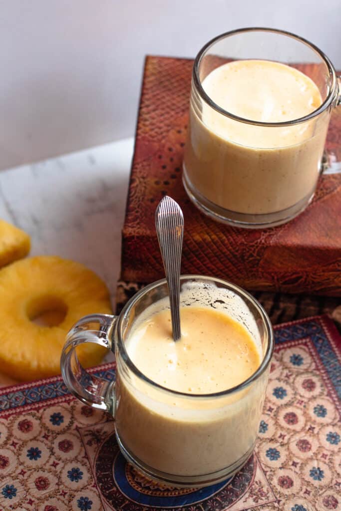 Two glasses of mango pineapple smoothie with pineapple slices, sitting on books