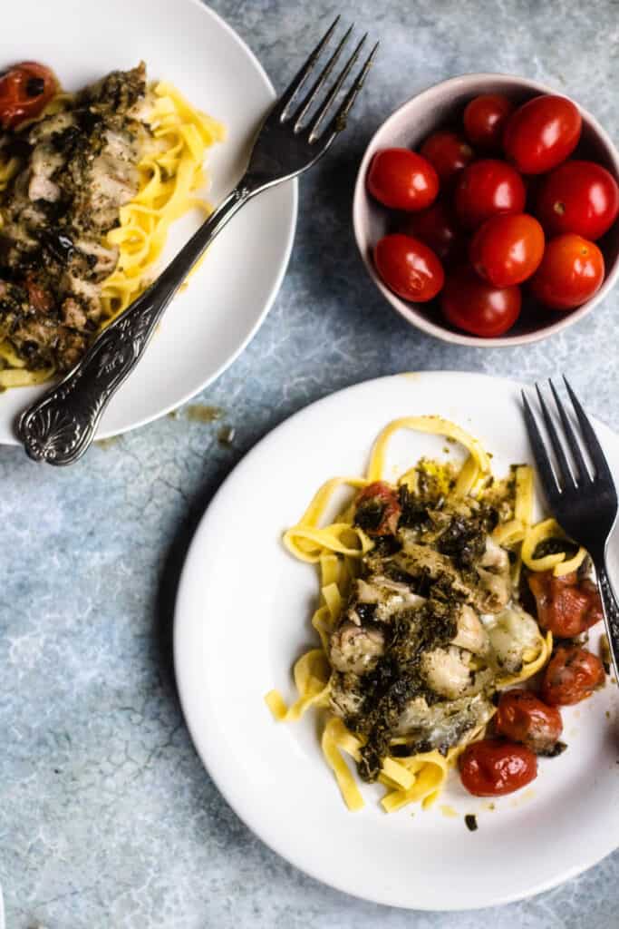 2 plates of pesto chicken with bowl of red cherry tomatoes 