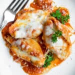 Three stuffed shells on a plate, sprinkled with parmesan cheese and topped with parsley.