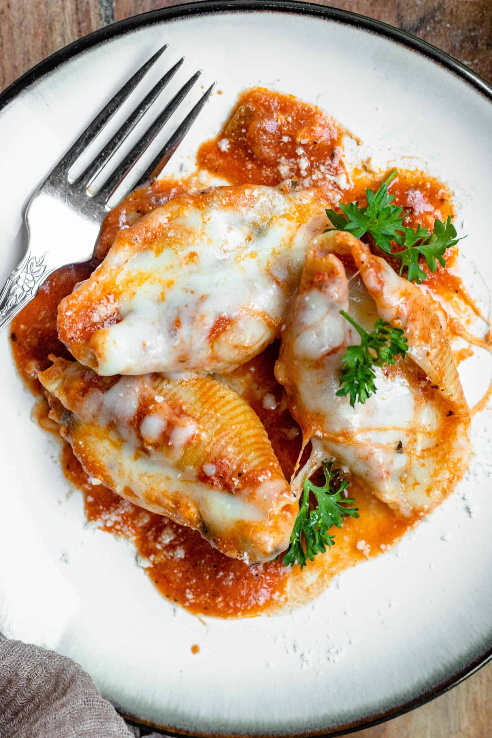 Three stuffed shells on a plate, sprinkled with parmesan cheese and topped with parsley.