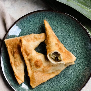 A green plate with 3 samosas on it, with a bite taken out of one.