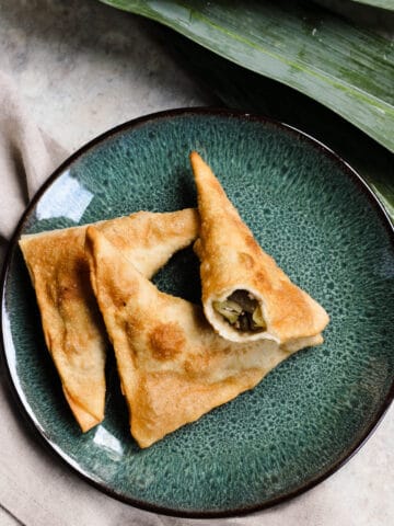 A green plate with 3 samosas on it, with a bite taken out of one.