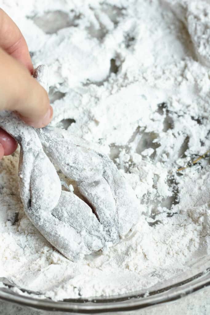 A hand dipping frog legs in flour 