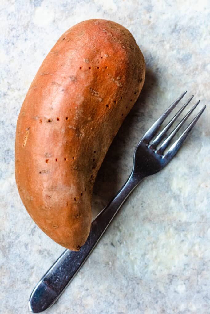 A sweet potato with pokes in the skin of the potato and a fork lying next to it. 