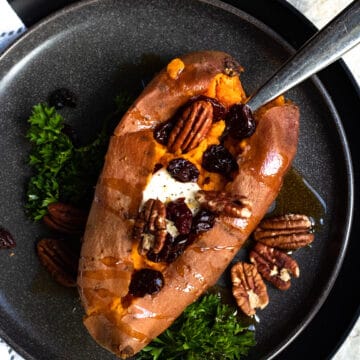 A baked sweet potato topped with pecans and cranberries with parsley on the side.