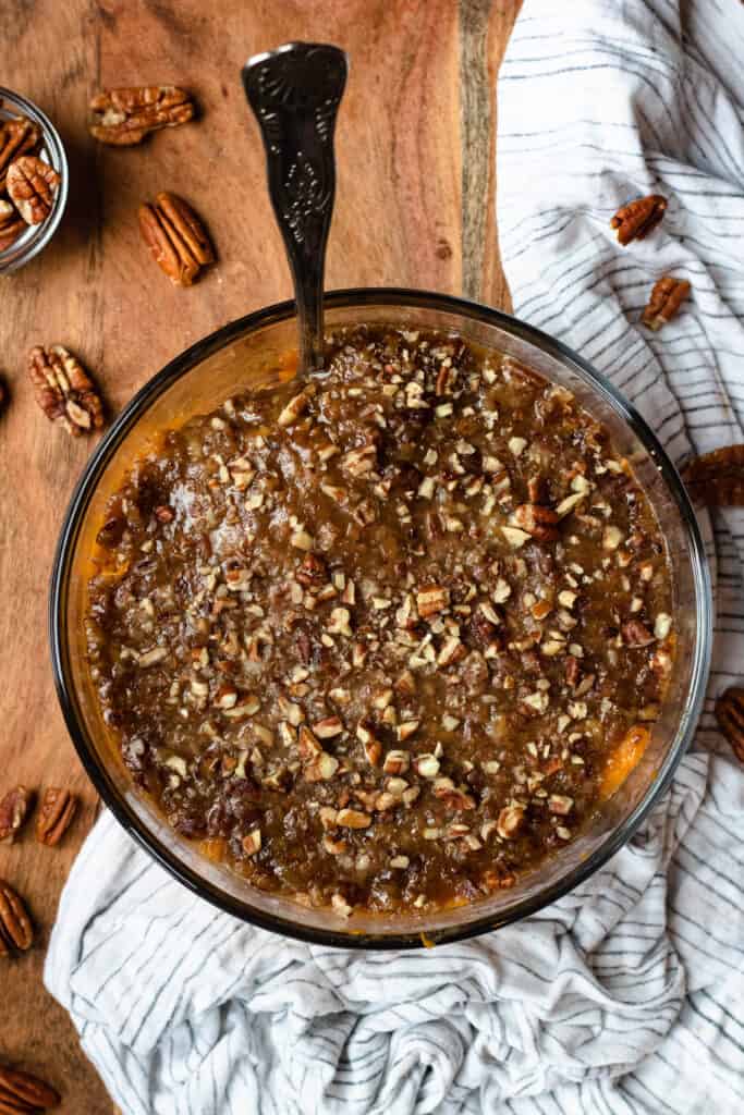 Cooked sweet potato casserole with a spoon in the casserole and surrounded by a linen and pecans.