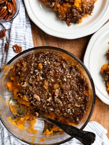 sweet potato casserole with a scoop taken out of it with two plates next to it, also filled with sweet potato casserole.